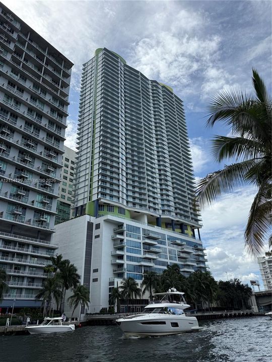 High-rise residential tower featuring a glass-facade exterior, tiered balconies, and water-front placement