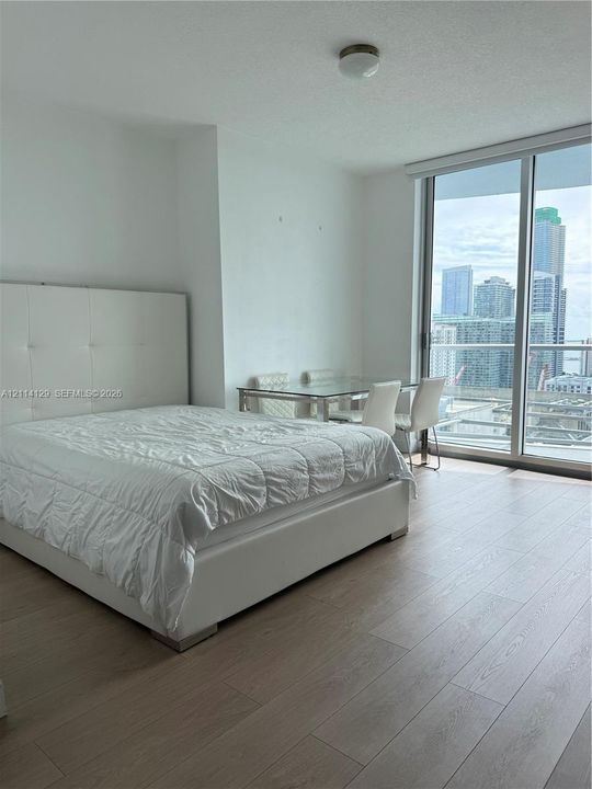 Floor-to-ceiling windows, wood-finish flooring, and a glass-paneled balcony door with urban skyline scenery