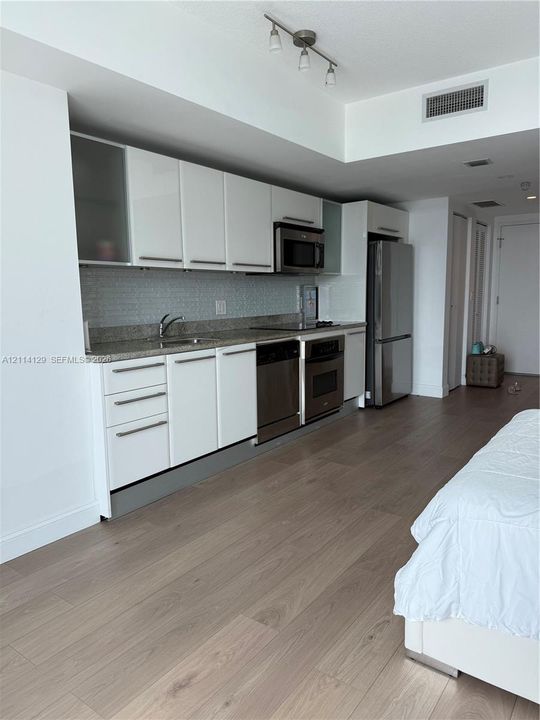 Kitchen featuring white cabinetry, stone-finish countertops, subway tile backsplash, and stainless steel appliances, complemented by wood-finish flooring