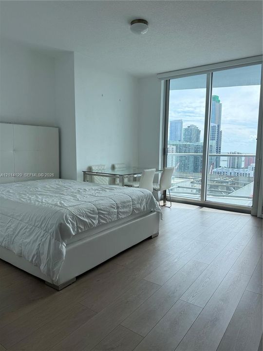 Floor-to-ceiling sliding glass doors, neutral wood-finish flooring, urban skyline scenery, and flush-mount ceiling lighting