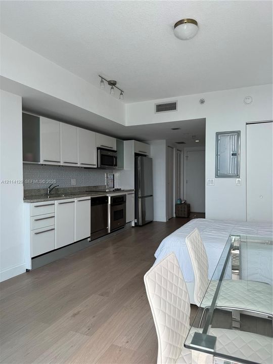 Kitchen featuring white cabinetry, stone-finish countertops, geometric tile backsplash, and stainless steel appliances, set against wood-finish flooring