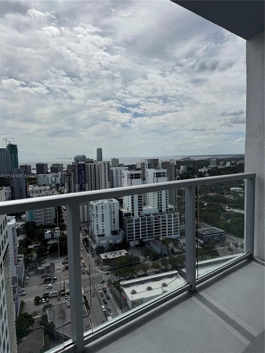 Covered balcony with a glass panel railing, offering expansive urban and coastal horizons