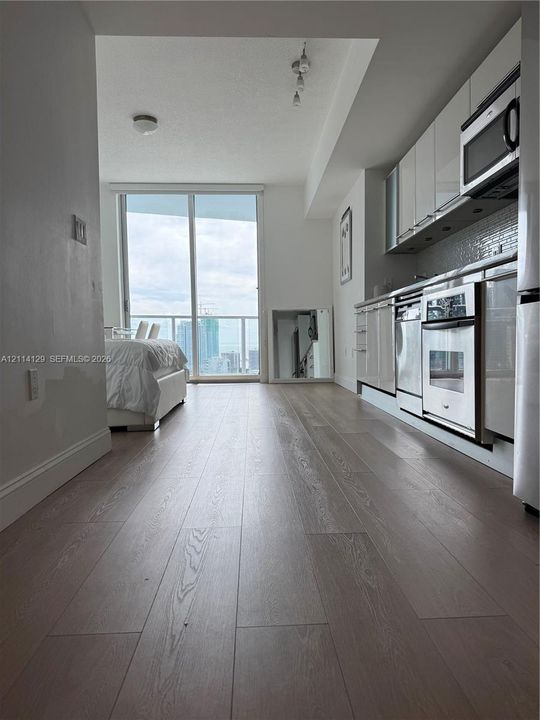 Kitchen featuring high-gloss cabinetry, stainless steel appliances, and tile backsplash, complemented by wide-plank wood-finish flooring and floor-to-ceiling glass sliding doors