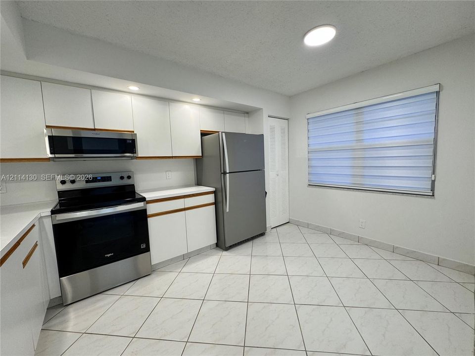 Kitchen featuring white flat-panel cabinetry, stainless steel appliances, ceramic tile flooring, and integrated lighting