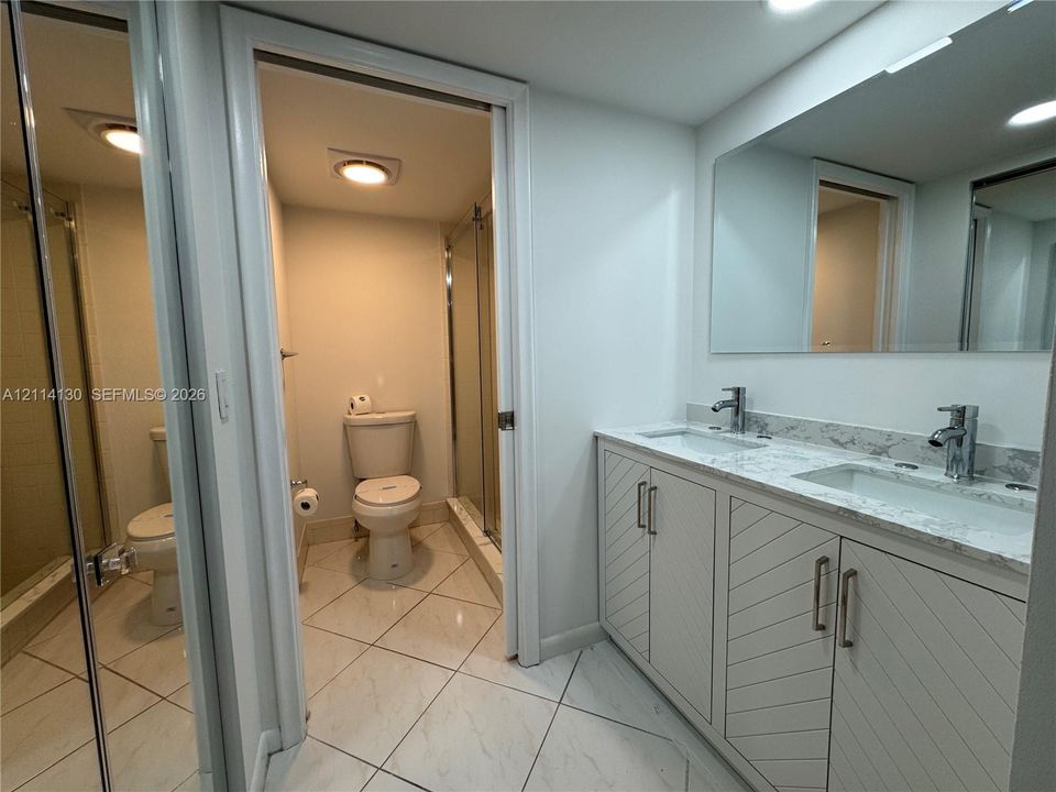 Dual-sink vanity with geometric cabinet detailing, light-toned stone-finish countertop, undermount sinks, polished chrome hardware, and large wall-to-wall vanity mirror