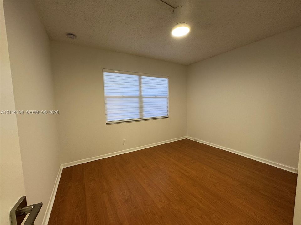 Room featuring wood-finish flooring, neutral wall paint, and a window with horizontal roller shades