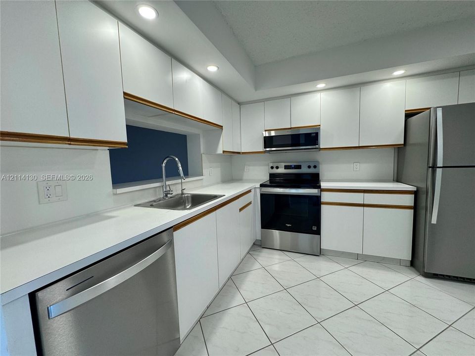 Kitchen featuring white cabinetry with integrated hardware, solid-surface countertops, stainless steel appliances, recessed ceiling lighting, and tile flooring