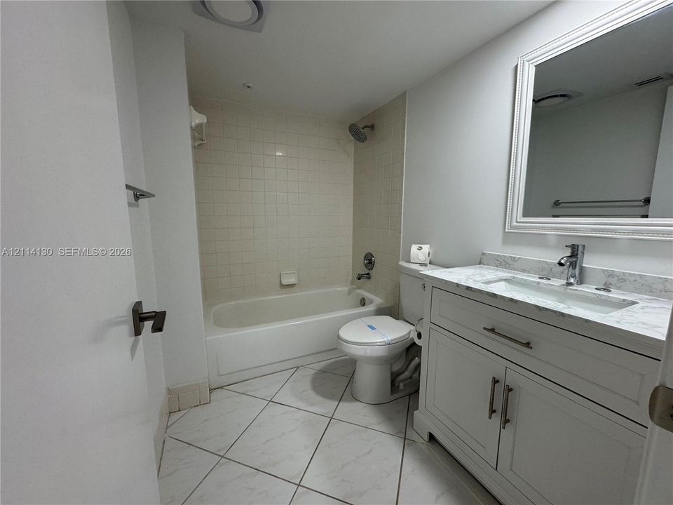 Bathroom featuring a white vanity with a stone-top integrated sink, square-tile tub surround, framed vanity mirror, and diagonal-pattern tile flooring