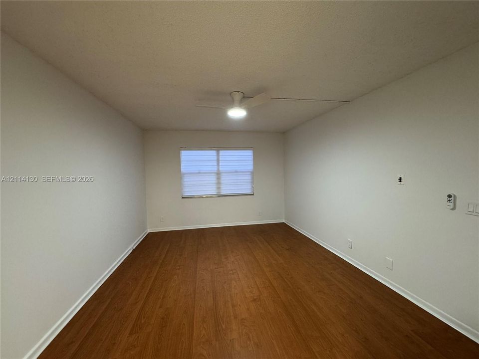 Interior space featuring wood-finish flooring, neutral wall tones, a central ceiling fan with integrated lighting, and a window with horizontal blinds