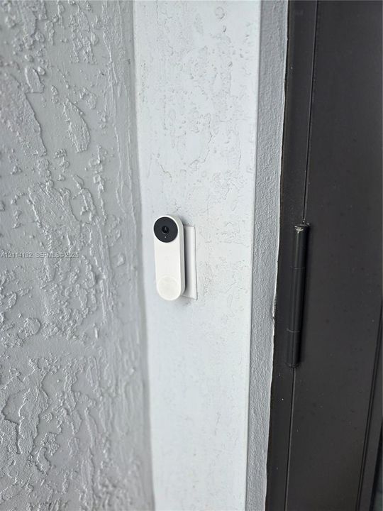 Integrated doorbell camera mounted on a textured exterior wall with a dark-finish door frame