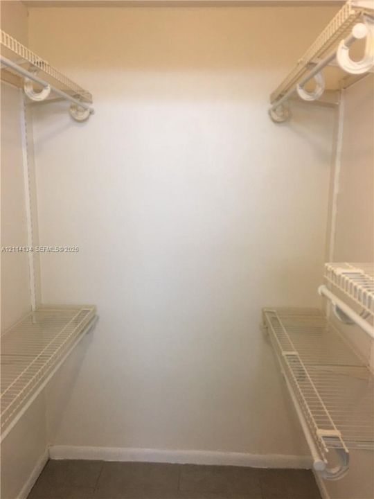 Walk-in storage space featuring dual-level white wire shelving and integrated hanging rods
