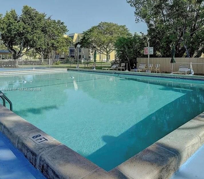 Rectangular swimming pool with stone coping, metal ladder, and paved deck area