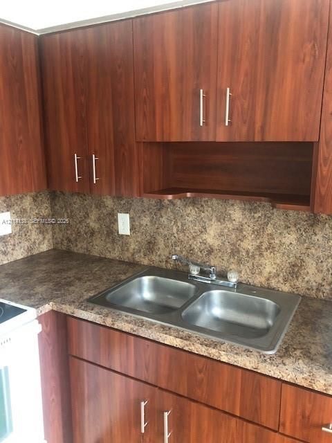Wood-finish cabinetry with silver-tone pulls, integrated open shelving, speckled laminate countertop, and a stainless steel double-basin sink with a dual-handle faucet