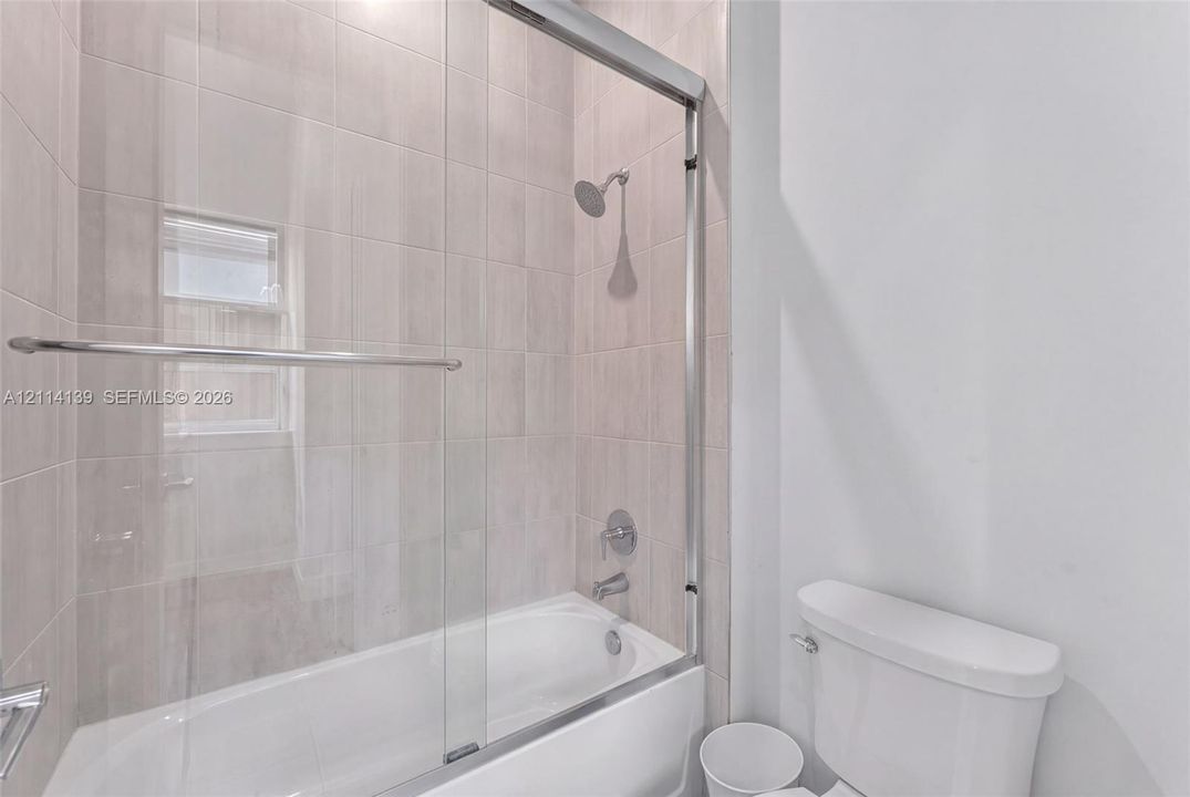 Full-height ceramic tile shower surround with a built-in recessed window, polished chrome shower fixtures, sliding glass shower door, and an acrylic bathtub