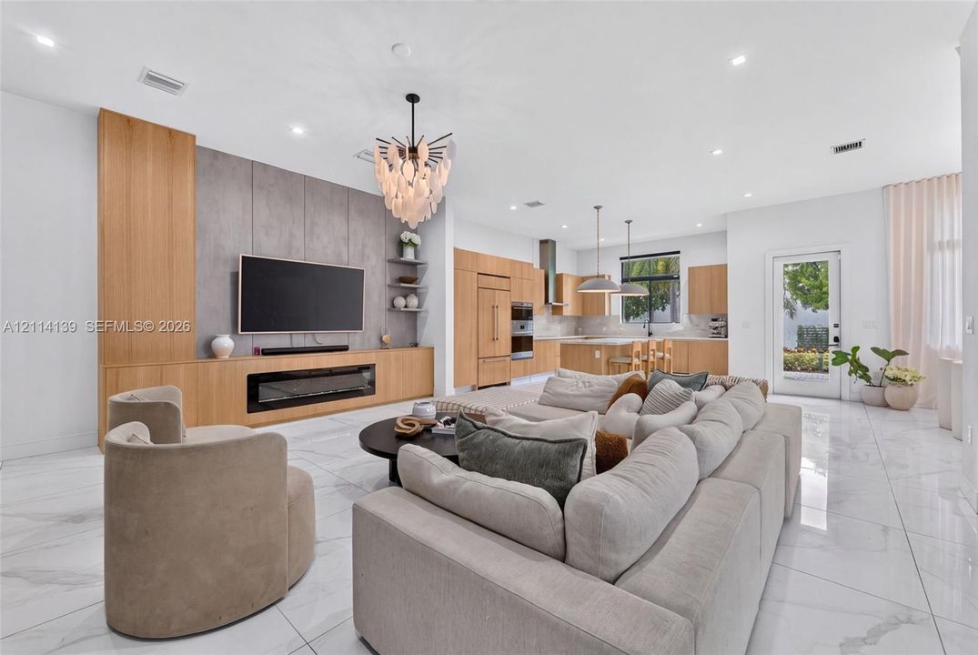 Large-format tile flooring, custom light-toned cabinetry, integrated fireplace, expansive stone-finish feature wall, and recessed ceiling lighting