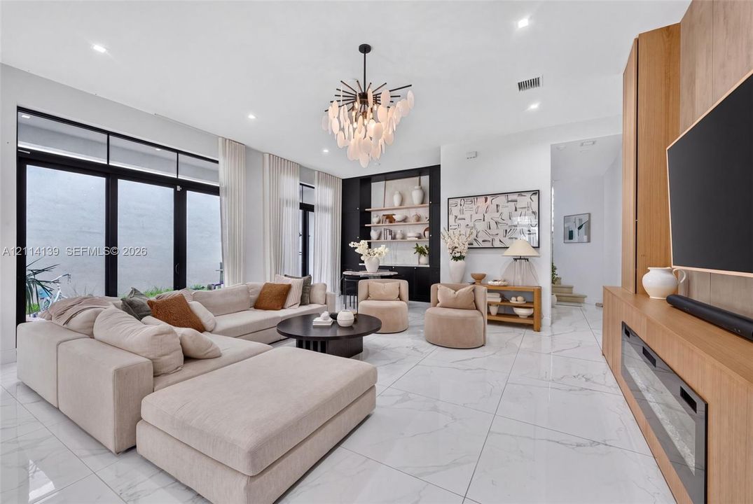 Living space featuring large-format tile flooring, floor-to-ceiling glass panel doors, a built-in wood-finish media console with an integrated fireplace, and custom built-in shelving