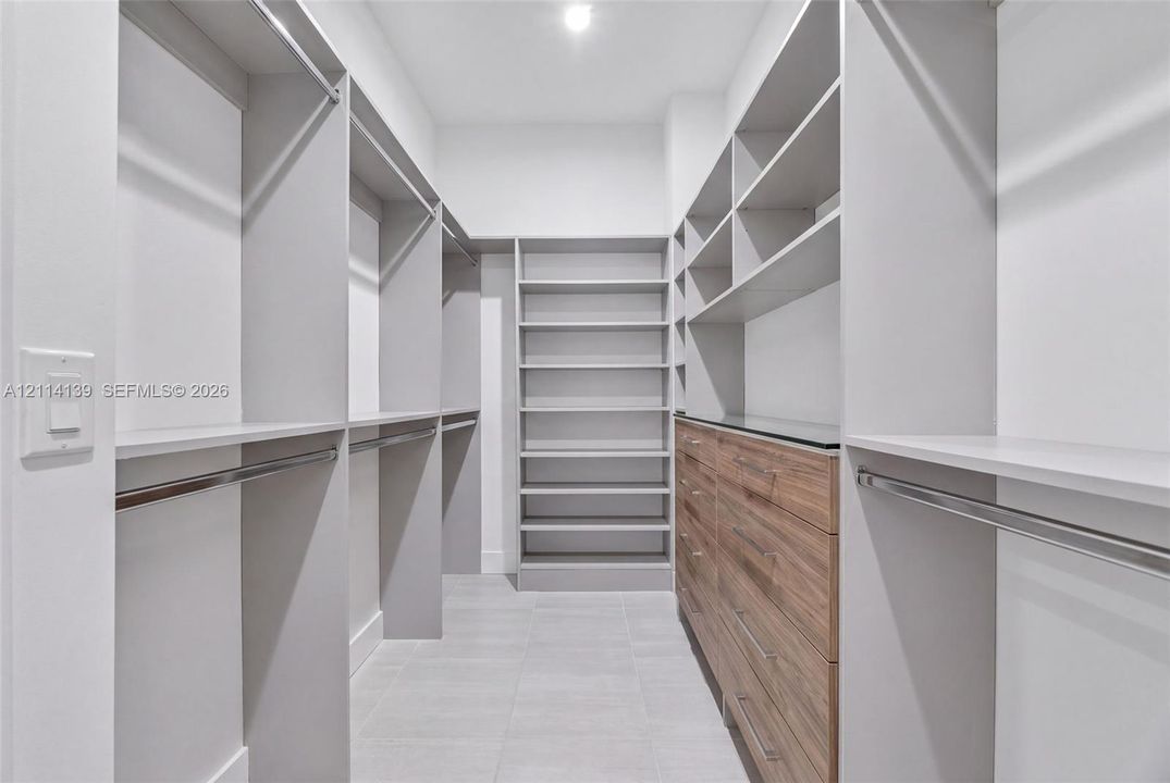 Walk-in closet featuring custom built-in shelving, wood-finish drawer cabinetry, metal hanging rods, and tiled flooring