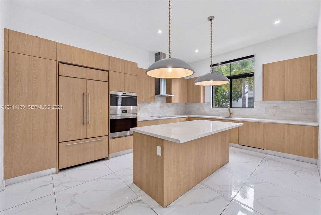 Kitchen featuring wood-finish cabinetry, quartz countertops, an oversized center island, built-in stainless steel appliances, and large-format tile flooring