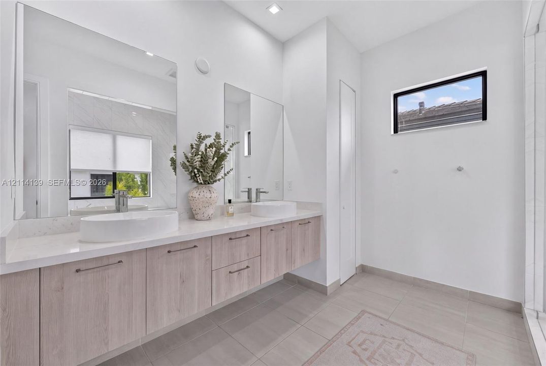 Floating vanity with wood-finish cabinetry, dual vessel sinks, solid-surface countertop, floor-to-ceiling mirrors, and rectangular transom window