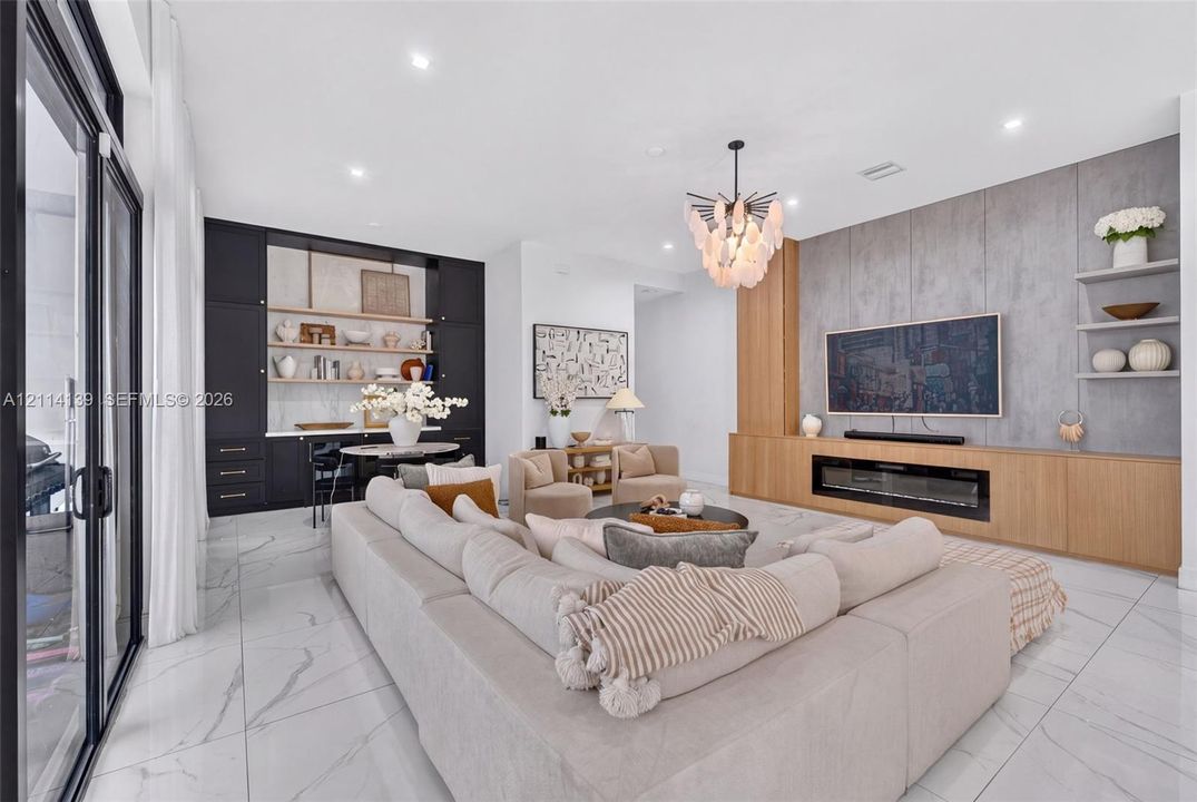 Living area featuring oversized floor-to-ceiling sliding glass doors, large-format tile flooring, a linear electric fireplace with wood-finish cabinetry, and recessed lighting