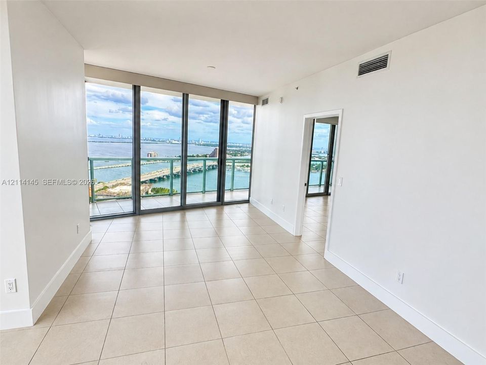 Floor-to-ceiling glass windows, ceramic tile flooring, and a private balcony featuring a glass railing with water and cityscape surroundings