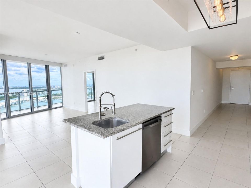 Kitchen island featuring stone countertop, undermount stainless steel sink, pull-down spray faucet, stainless steel dishwasher, and white cabinetry