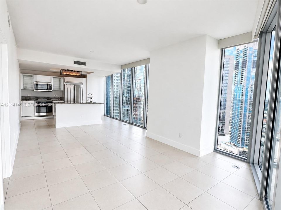 Open-concept kitchen featuring stainless steel appliances, white cabinetry, and stone-surface countertops, complemented by floor-to-ceiling windows and tile flooring