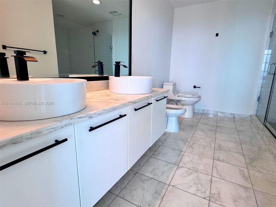 Double vanity featuring stone-finish countertops, dual vessel sinks, matte black fixtures, and white cabinetry, complemented by stone-finish floor tiling