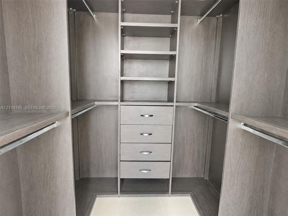 Custom closet organization system featuring wood-finish cabinetry, four integrated storage drawers with brushed metal pulls, adjustable shelving, and multiple hanging rods
