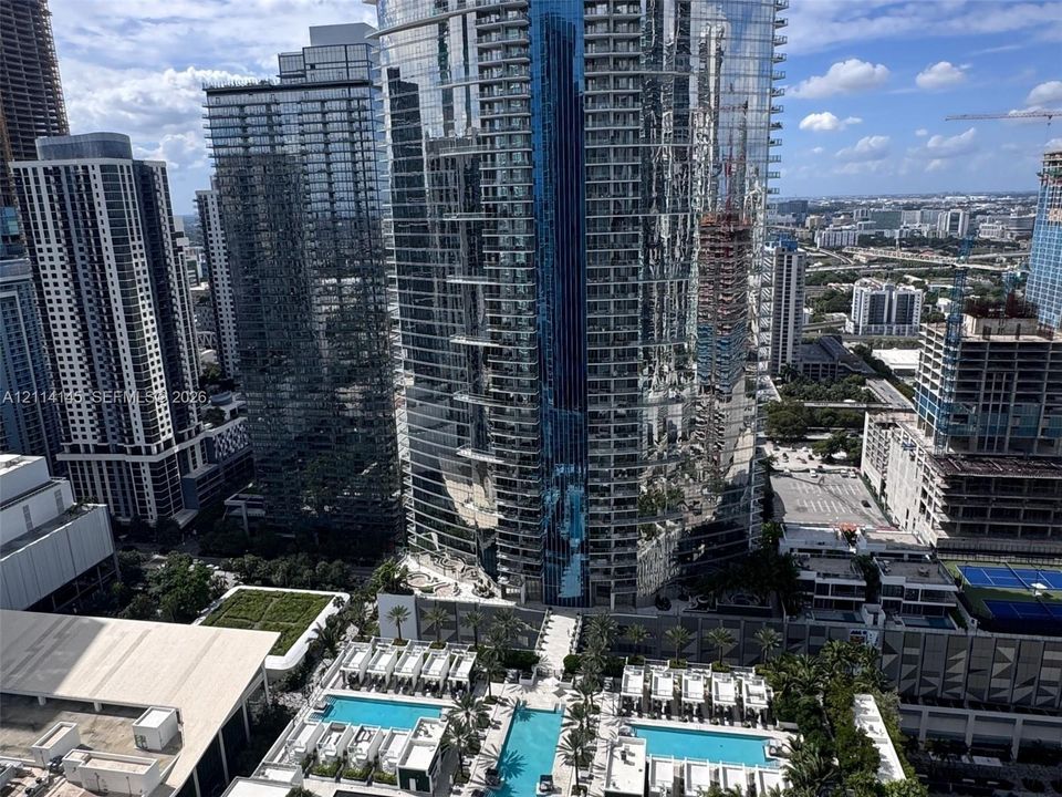High-rise urban setting featuring tiered swimming pools, landscaped terrace areas with palm trees, and glass-façade architecture