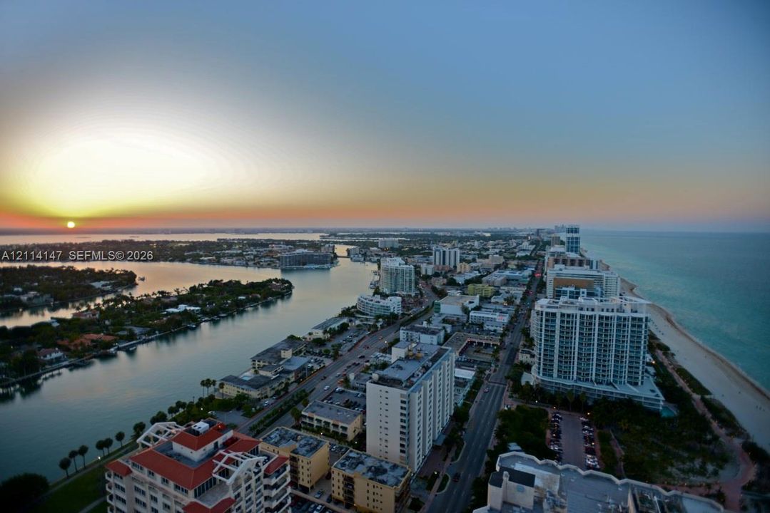 High-altitude coastal panorama featuring an expansive shoreline, an inlet waterway, and sunset horizon