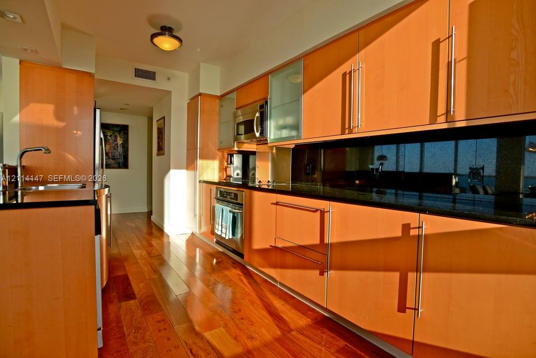 Kitchen featuring flat-panel wood cabinetry, black countertops, stainless steel appliances, and wood-finish flooring
