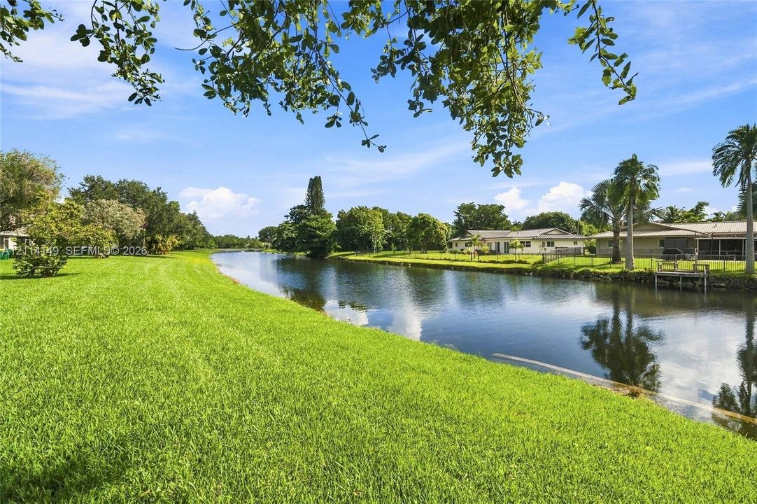 Waterfront property featuring a manicured lawn, canal access, and a wooden dock