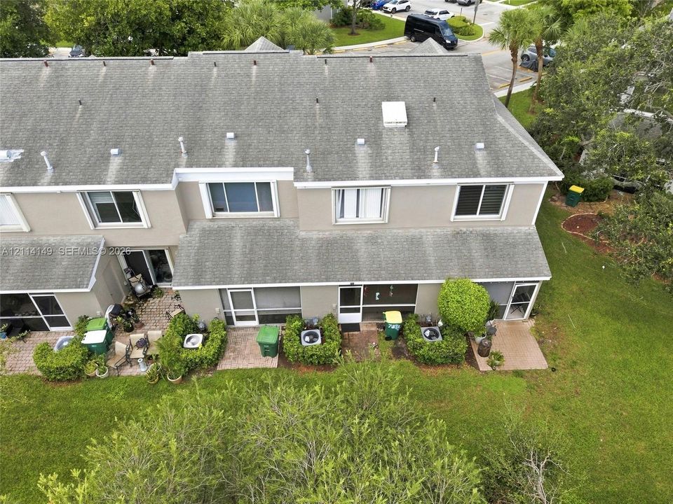Exterior view of a multi-unit property featuring a shingled roof, stucco siding, individual paved patios, and designated green space