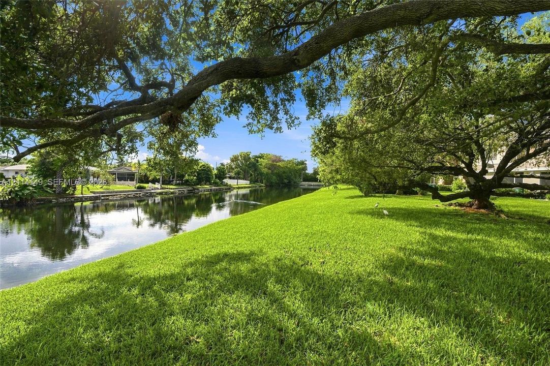 Waterfront lot featuring a wide canal, expansive lawn, and mature oak trees