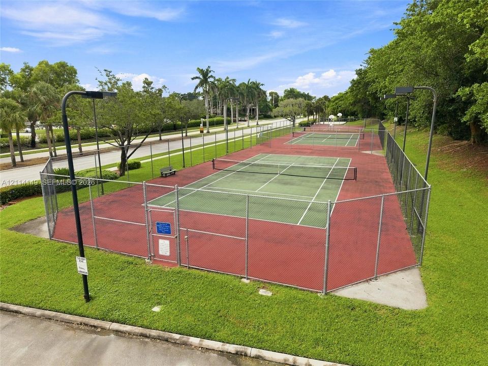Two fenced hard-court tennis courts featuring court lighting, integrated nets, and perimeter chain-link fencing