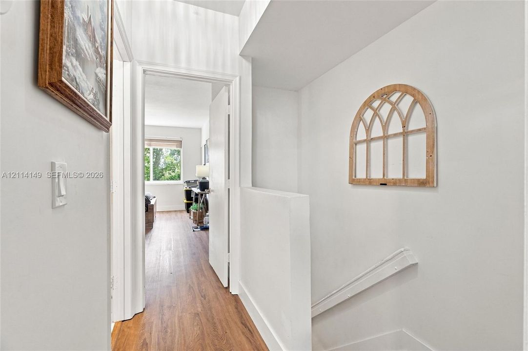 Hallway featuring wood-finish flooring, white walls, and a recessed arch-top wall niche