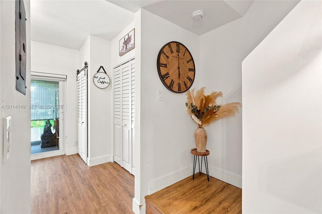 Entryway featuring wood-finish flooring, white louvered-style closet doors, a sliding barn-style door, and a glass-paneled exterior door