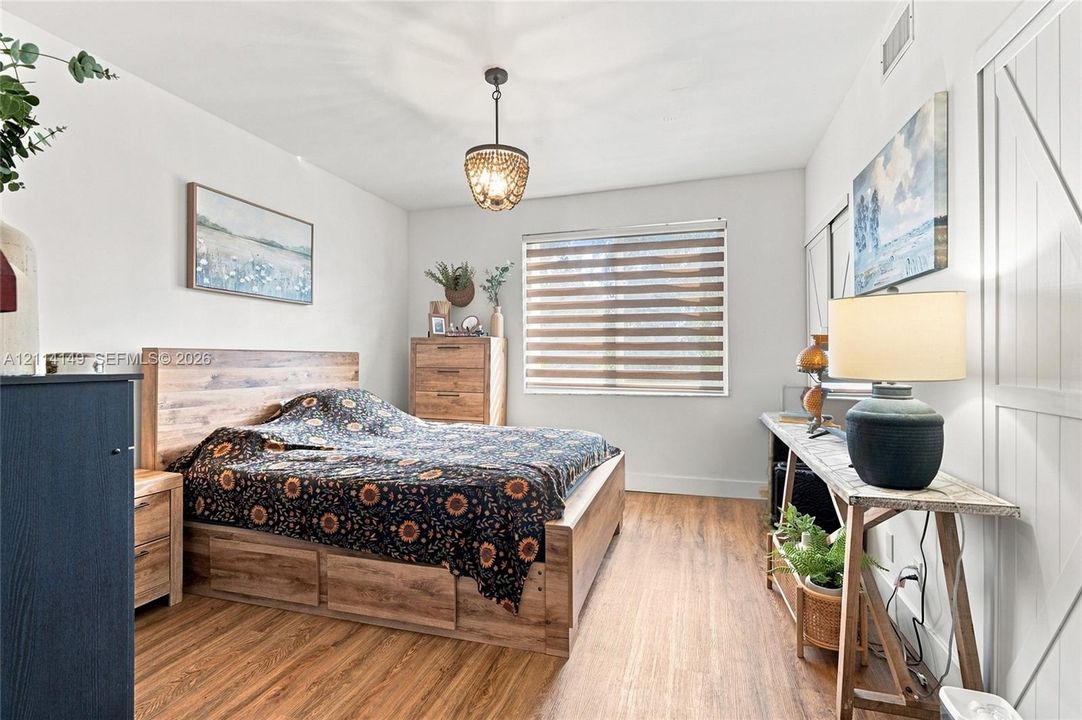 Wood-finish flooring, wood-toned paneled sliding barn door, bead-accented pendant light fixture, and horizontal-slat window treatments