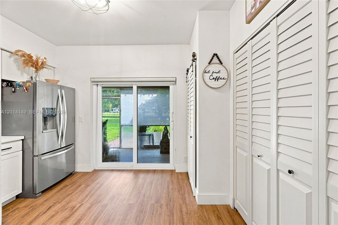 Kitchen area featuring wood-finish flooring, white cabinetry, stainless steel refrigerator, louvered bi-fold closet doors, and a sliding glass door