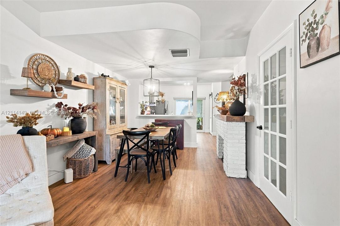 Wood-finish flooring, white painted brick fireplace with wood mantel, custom curved ceiling soffit, and multi-light French door