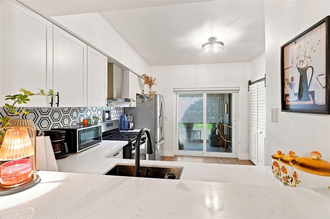 Kitchen featuring white shaker-style cabinetry, quartz countertops, a geometric patterned backsplash, stainless steel appliances, and a matte black gooseneck faucet