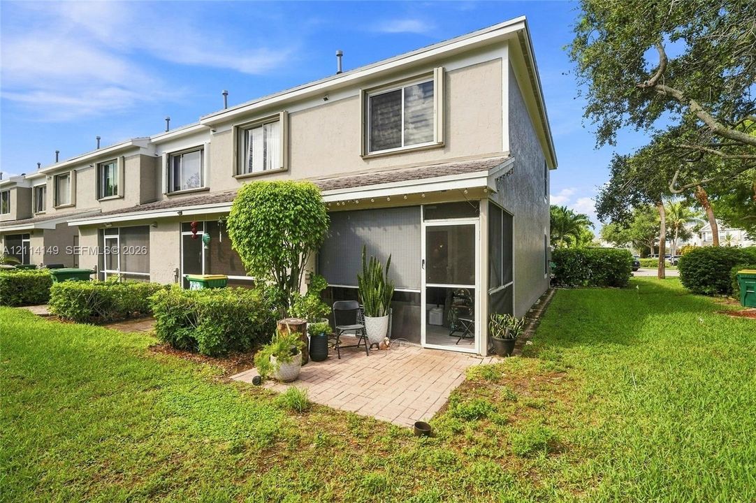 Exterior featuring a stucco facade, screened-in patio, brick-paver patio area, and mature landscaping