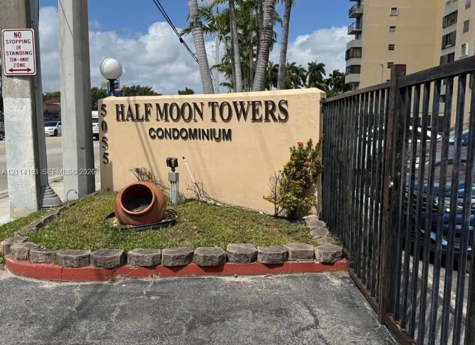Property signage featuring stucco masonry, stone-edged landscaping, and a metal security gate