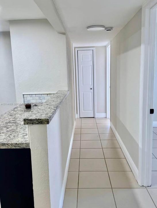 Hallway featuring large-format ceramic tile flooring, a stone-finish countertop, and a white six-panel interior door