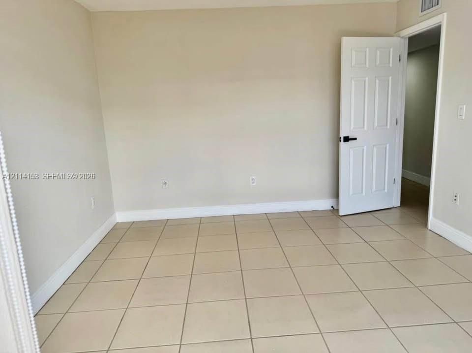 Neutral-toned interior space featuring light-colored tile flooring, smooth walls, and a six-panel door with matte black hardware