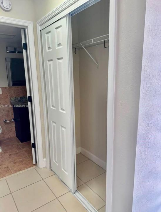 Sliding panel closet doors with white six-panel design, interior shelving, and neutral floor tile