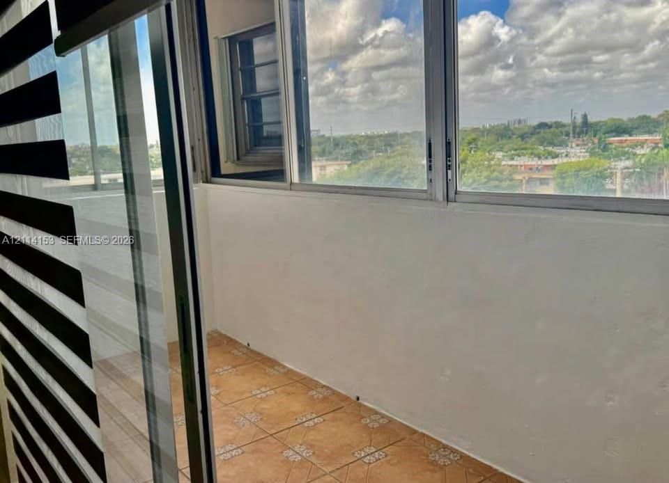 Enclosed balcony featuring tile flooring, expansive window panels, and a sliding glass door with striped light-filtering shades