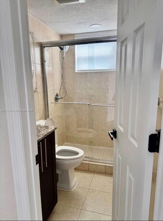 Walk-in shower with sliding glass doors, floor-to-ceiling tile surround, dark wood-finish vanity, stone countertop, and recessed ceiling lighting
