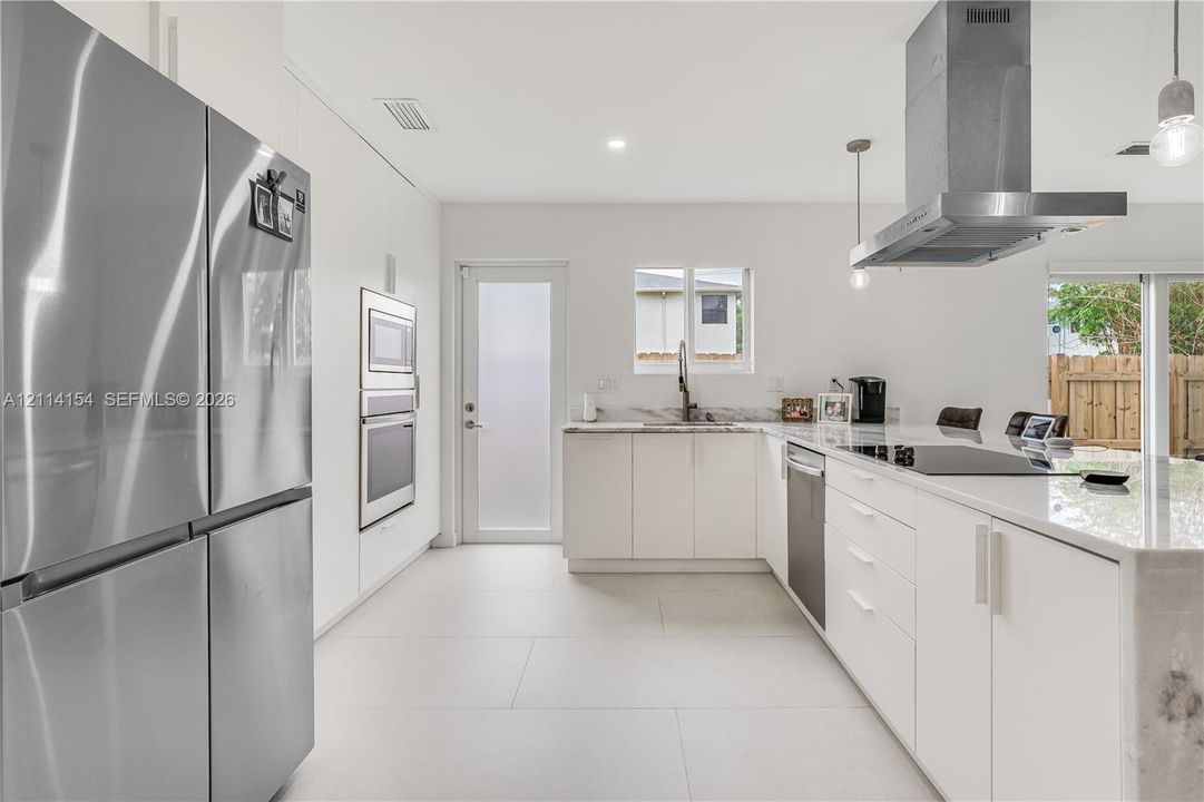 Modern kitchen featuring flat-panel cabinetry, stone countertops, stainless steel appliances, a chimney-style range hood, and large-format tile flooring